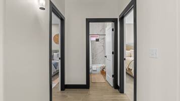 A hallway with a mirrored wall, leading to a bathroom with a marble wall and a bathtub.