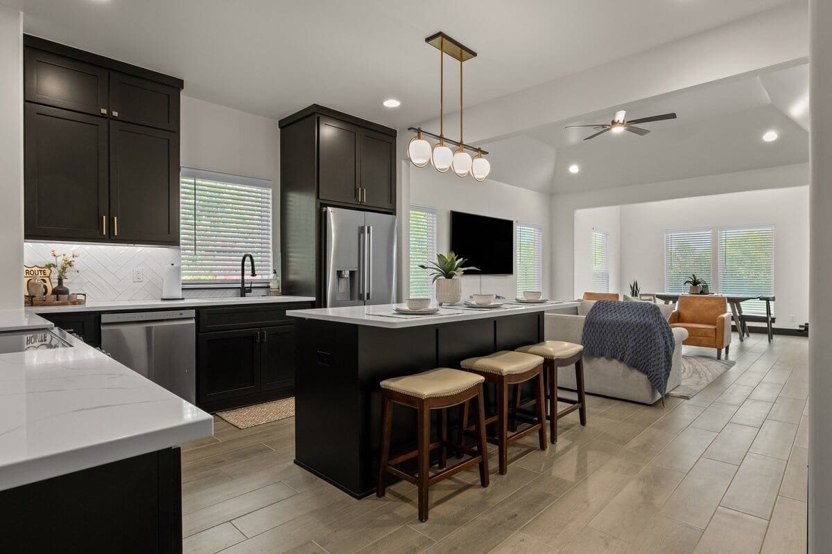 A modern kitchen with dark cabinetry, a central island with stools, a built-in refrigerator, and a ceiling fan.