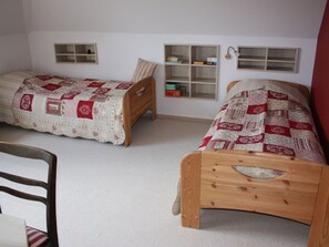 A room with two wooden beds, each with a quilted bedspread. There are two small shelves with books and a lamp on the wall. - Holiday Apartment With 1 Bedroom (Oldsum)