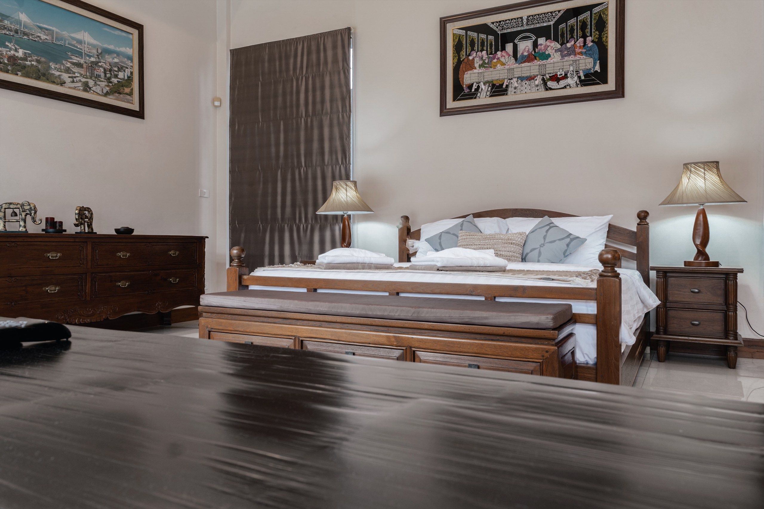 Habitación de hotel con cama de madera, dos lámparas de noche, una mesita de noche, un aparador y dos cuadros en la pared.