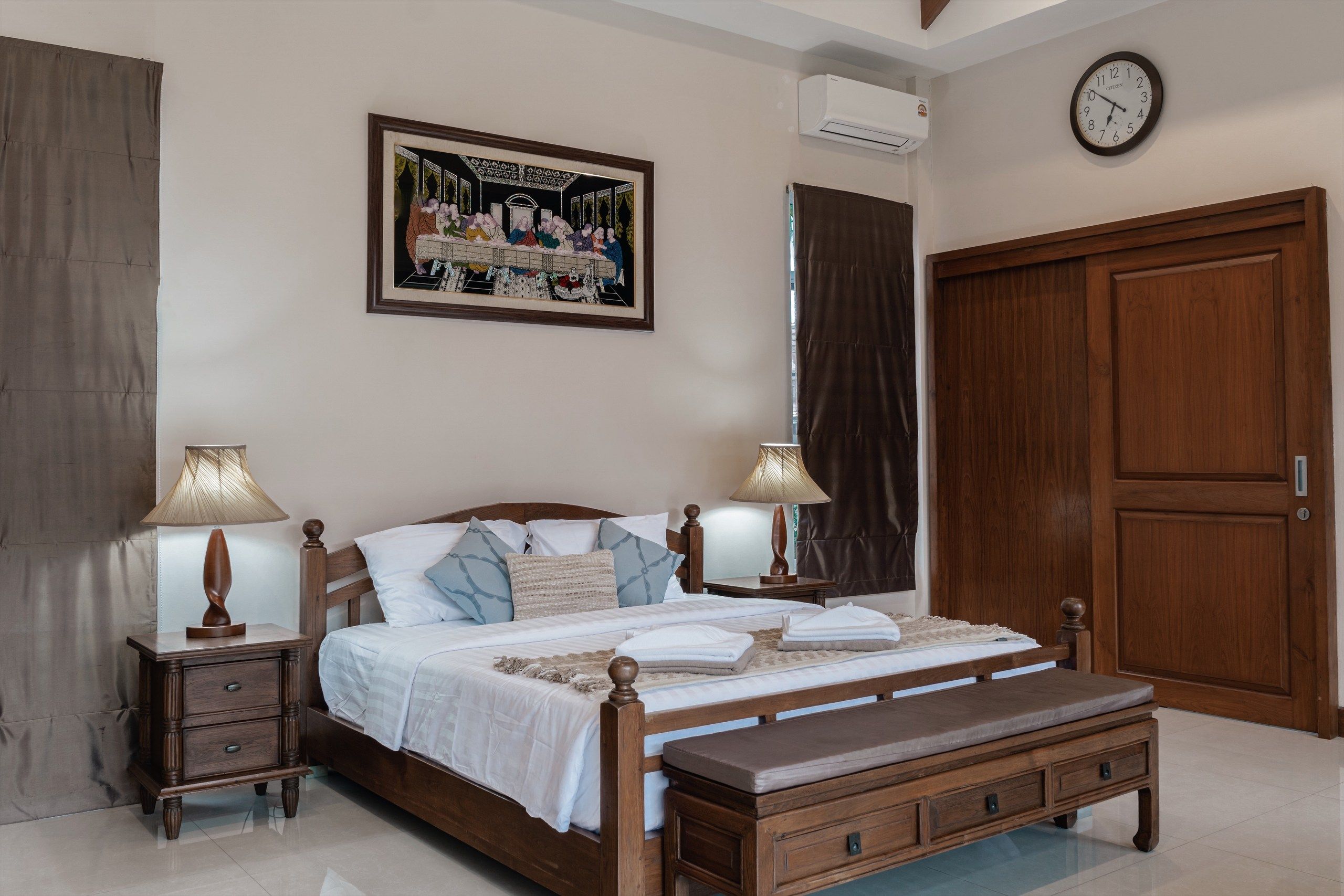 A bedroom with a wooden bed, two bedside tables with lamps, a large wooden wardrobe, and a painting on the wall.