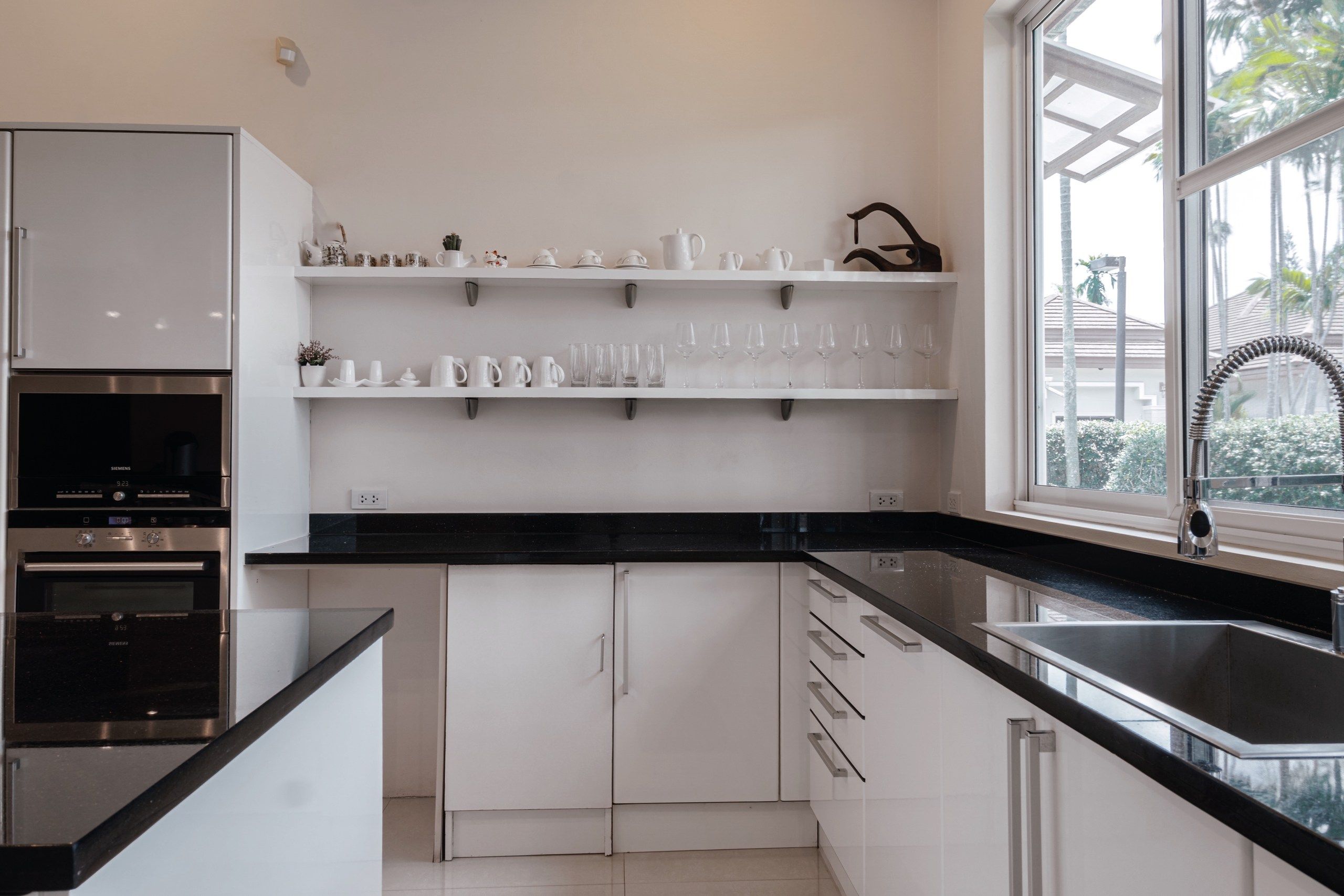 Una cocina moderna con armarios blancos, encimeras negras y una ventana con vista a palmeras.