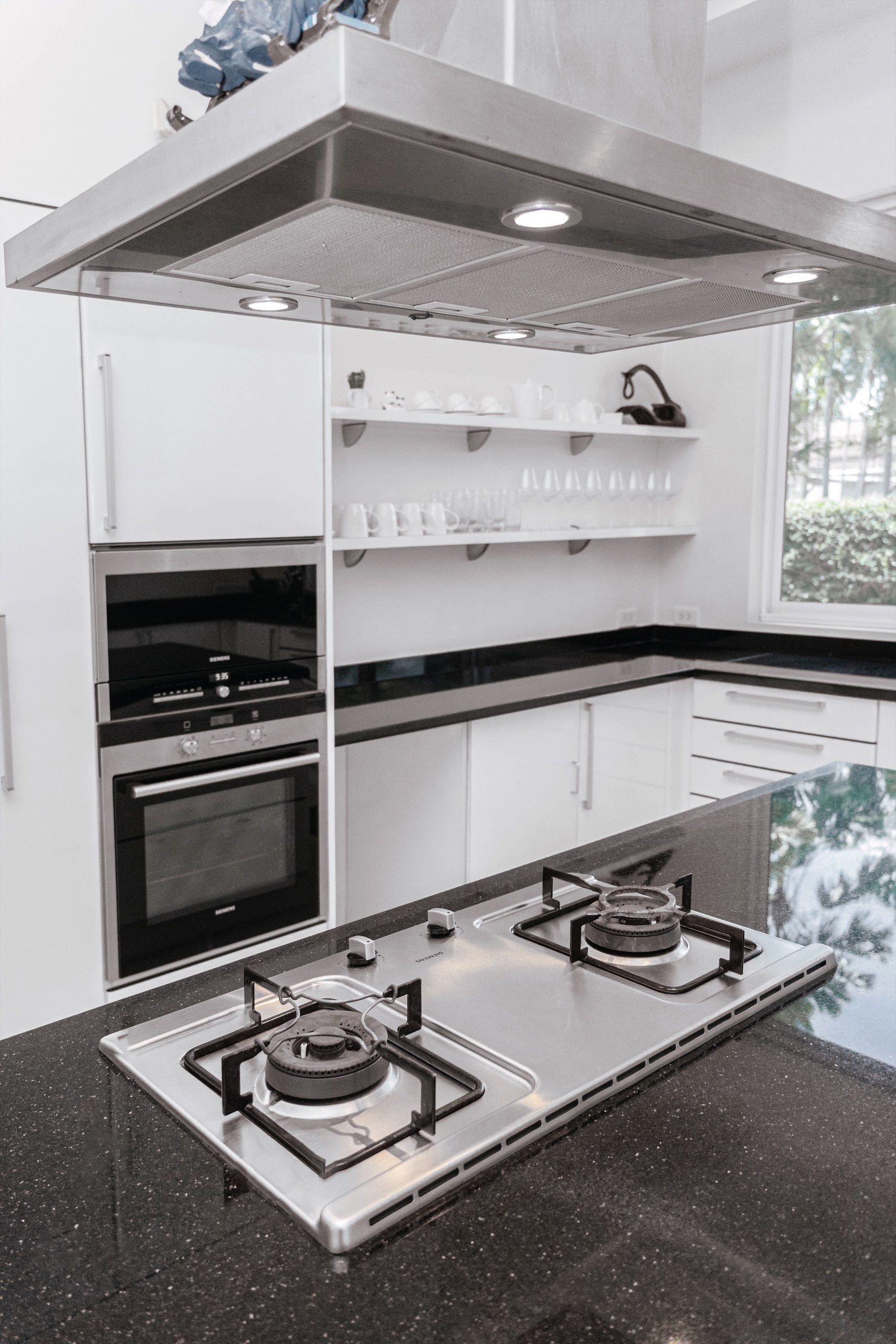 Une cuisine moderne équipée d’appareils électroménagers en acier inoxydable, notamment une cuisinière à gaz à deux brûleurs, un four encastré et un four à micro-ondes.