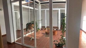 Quarto com porta de vidro deslizante que dá para um pátio externo com plantas em vasos e piso ladrilhado.