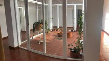 Ein Zimmer mit einer Schiebetür, die auf eine Terrasse mit Topfpflanzen und einem gefliesten Boden führt.