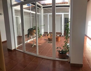 Ein Zimmer mit einer Schiebetür, die auf eine Terrasse mit Topfpflanzen und einem gefliesten Boden führt.