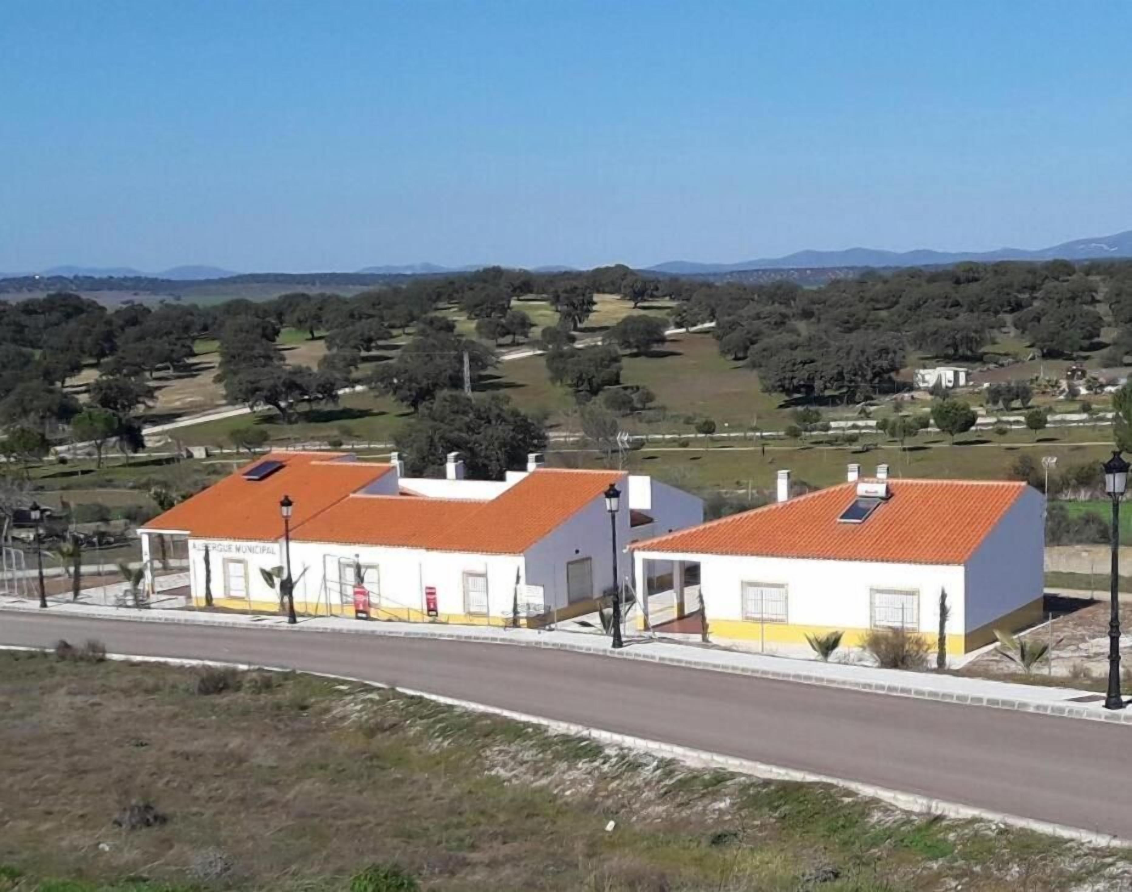 A rural setting with two white buildings with red roofs, a paved road, and a hilly landscape in the background.