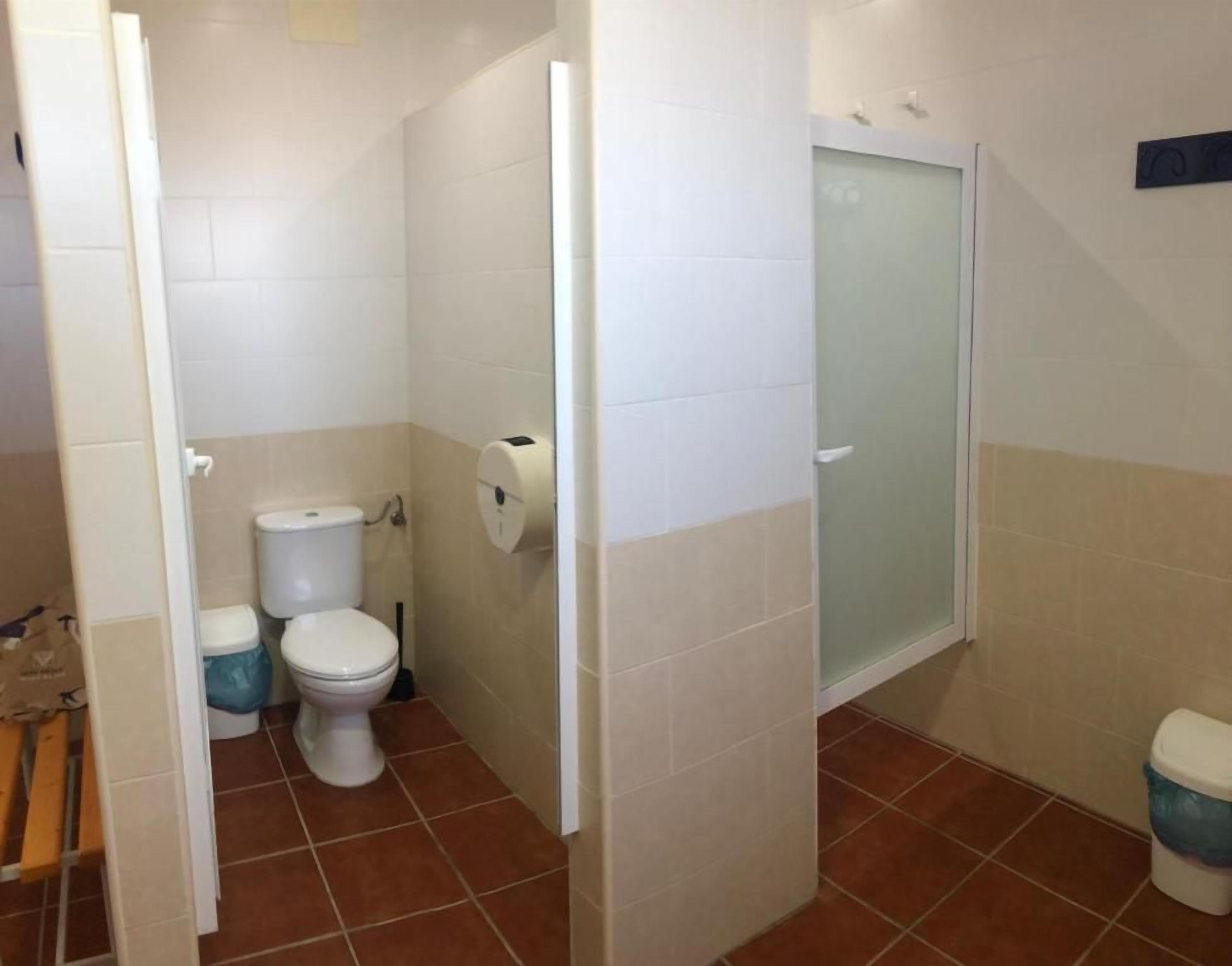 A bathroom with a toilet, a shower enclosure, and a trash bin.
