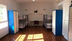 Um dormitório com beliches, uma mesa e uma janela.