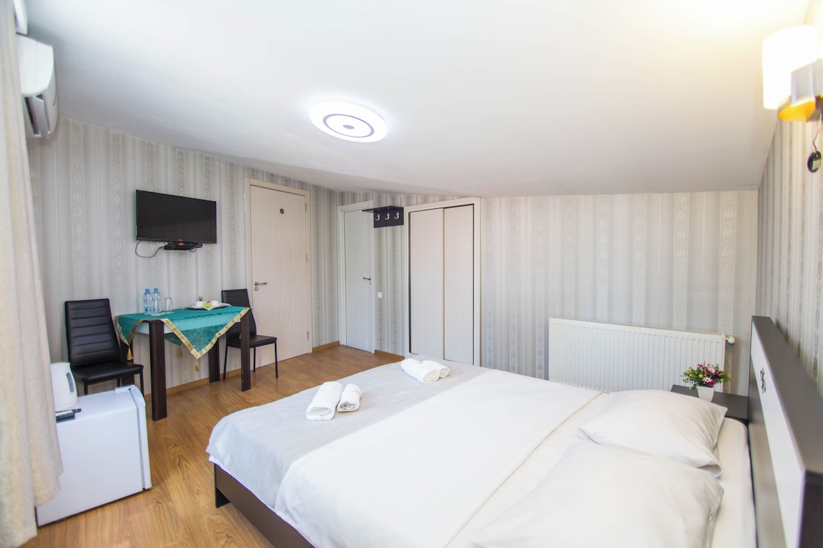 A hotel room with a bed, a desk with a chair, a television, and a wardrobe.