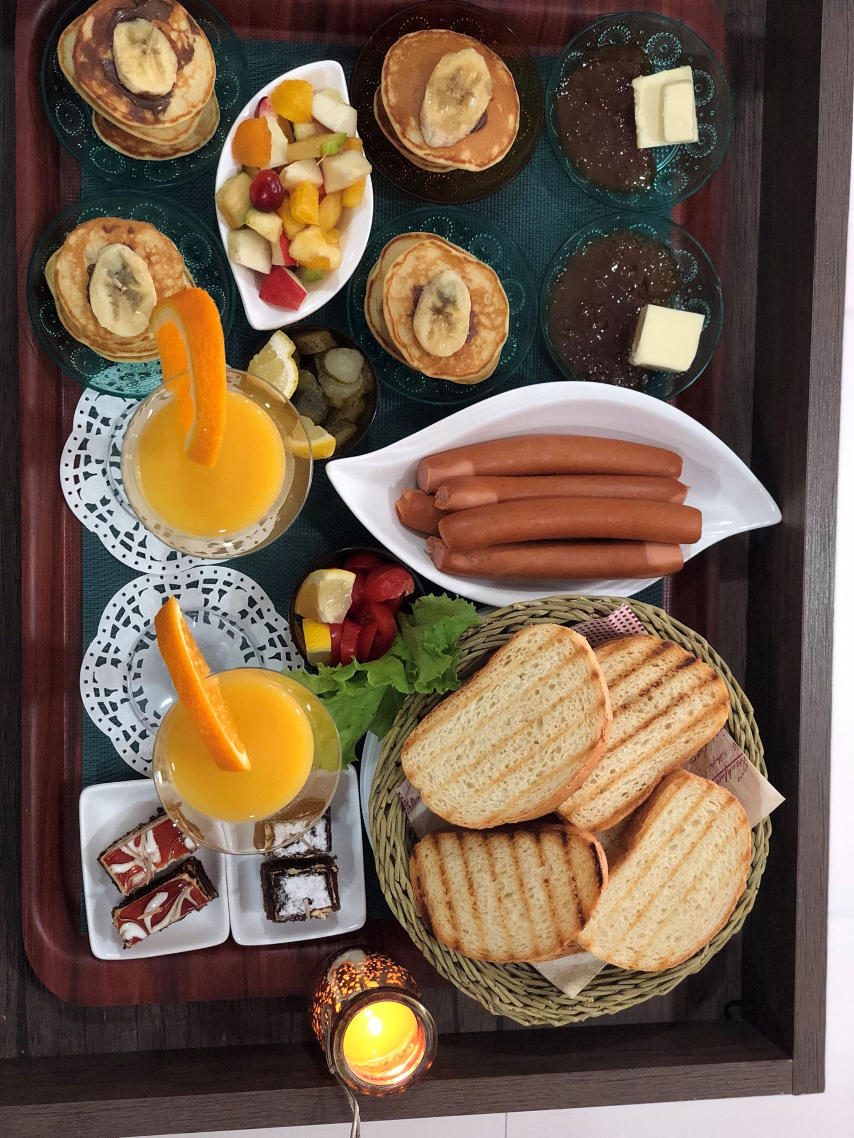 A tray with pancakes, hot dogs, fruit, bread, and a candle.