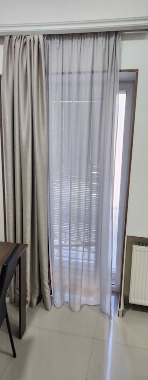 A room with a window covered by sheer curtains, a radiator, and a table with a chair. - Old Georgia (Tbilisi)