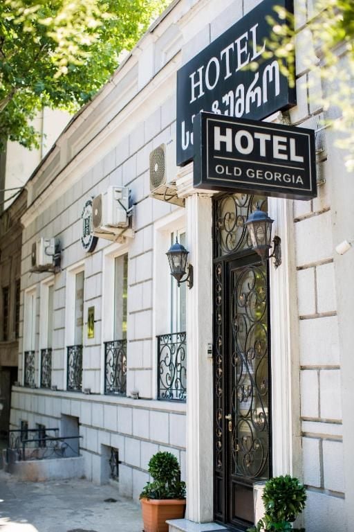 Entrada de un hotel con una puerta de hierro forjado negro y señalización que indica 'HOTEL & HOTEL' y 'HOTEL OLD GEORGIA'.
