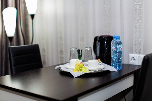A hotel room with a dining table set with a white cup, a flower, and two bottles of water.