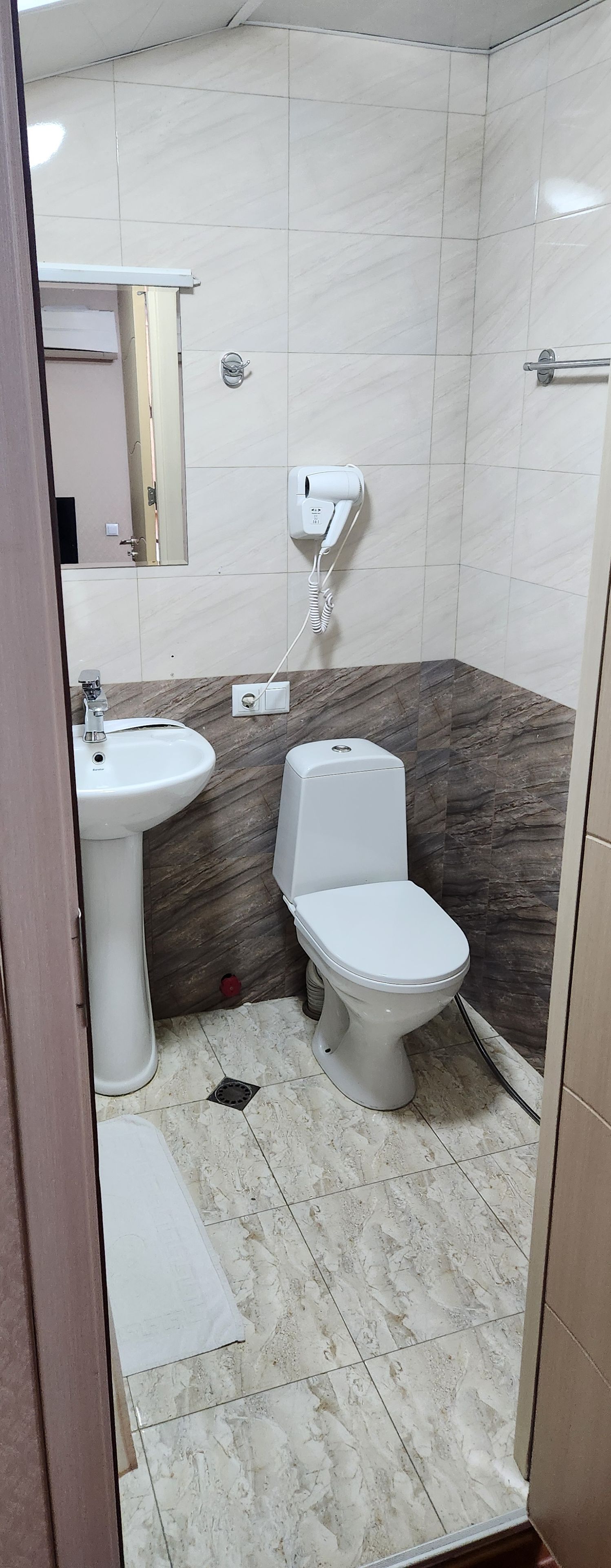 A bathroom with a white sink, toilet, and a hairdryer mounted on the wall.