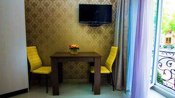 A room with a television mounted on the wall, a table with two chairs, and a window with curtains.