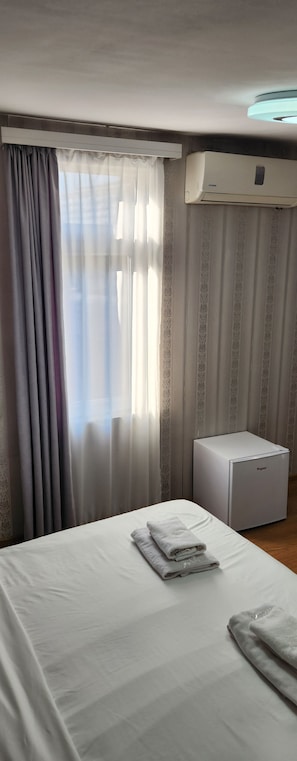 A hotel room with a bed, a radiator, and a window with curtains.