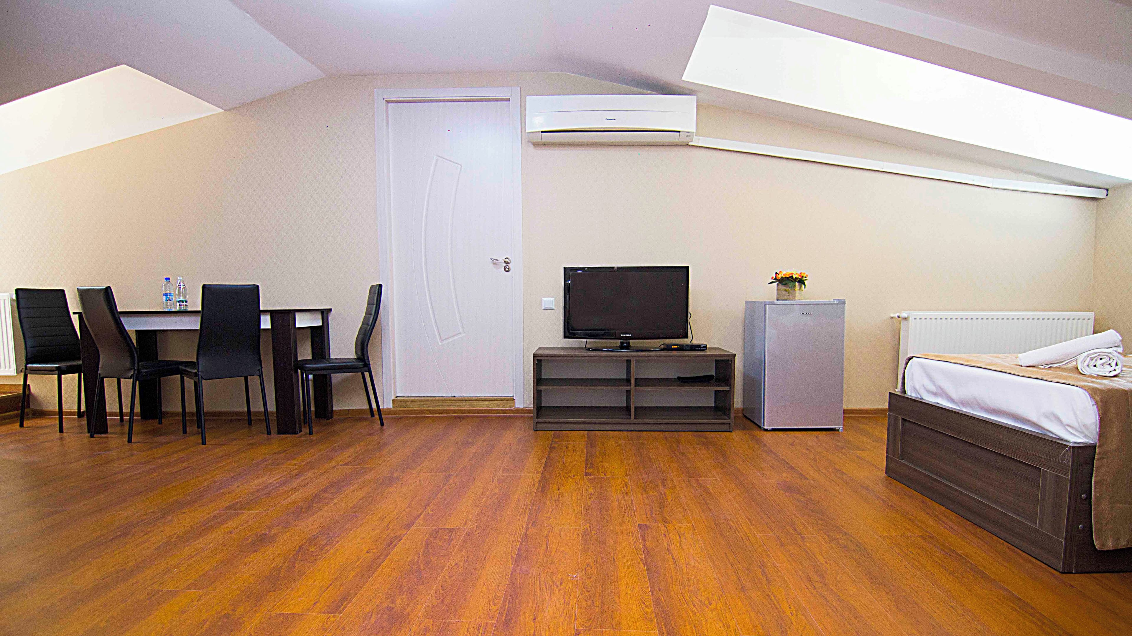A room with a dining table, chairs, a TV, a refrigerator, and a bed.