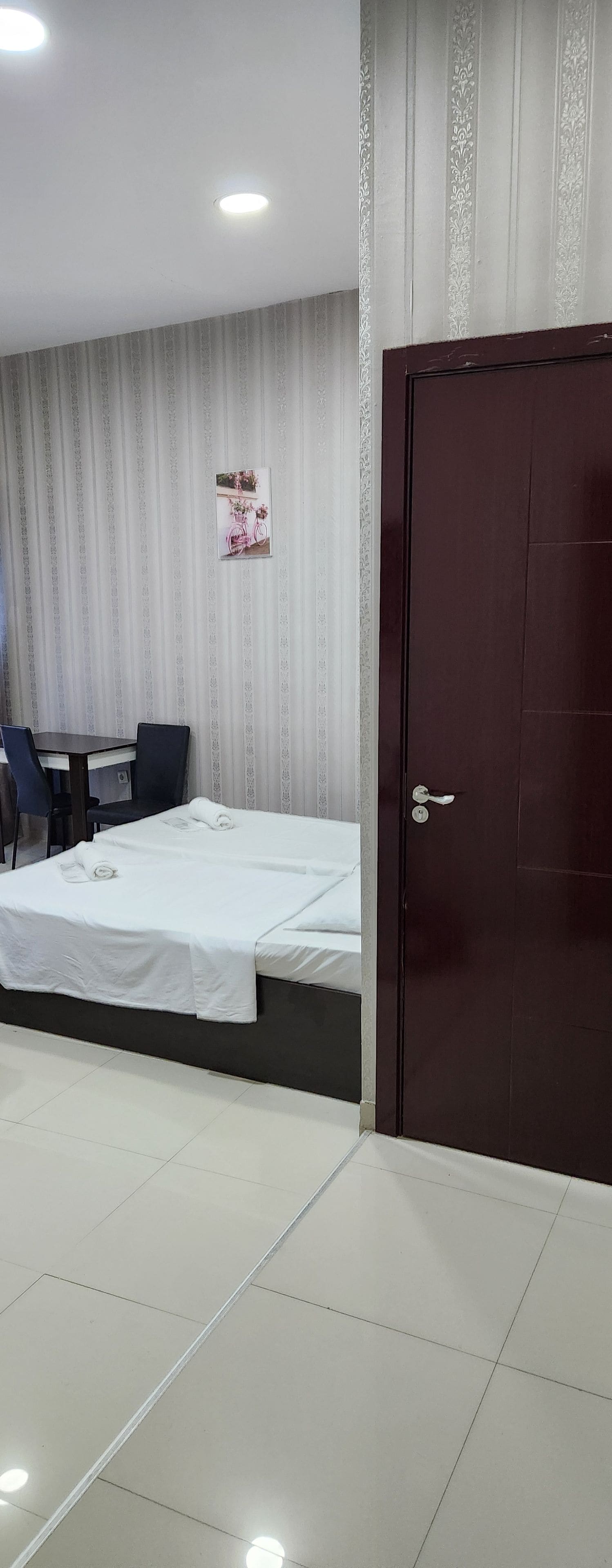 Una habitación de hotel con una cama, un escritorio, dos sillas, una puerta y una cortina estampada.