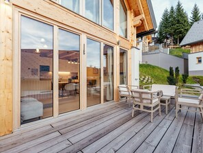 Eine Holzdielen-Terrasse mit Gartenmöbeln, ein Glastür-Eingang und Blick ins Innere.