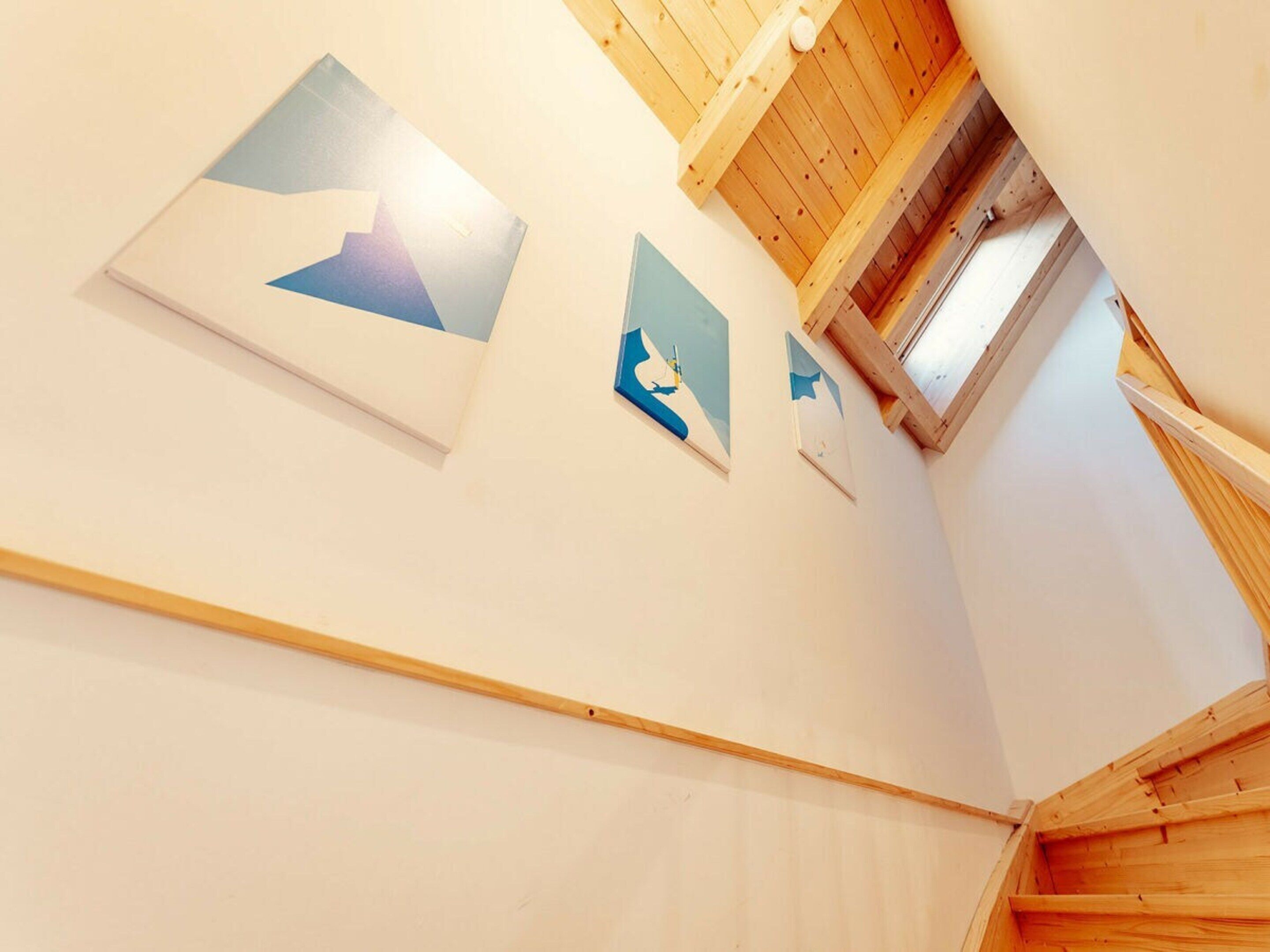 A corridor with wooden beams and a sloped ceiling, leading to a room with a skylight.