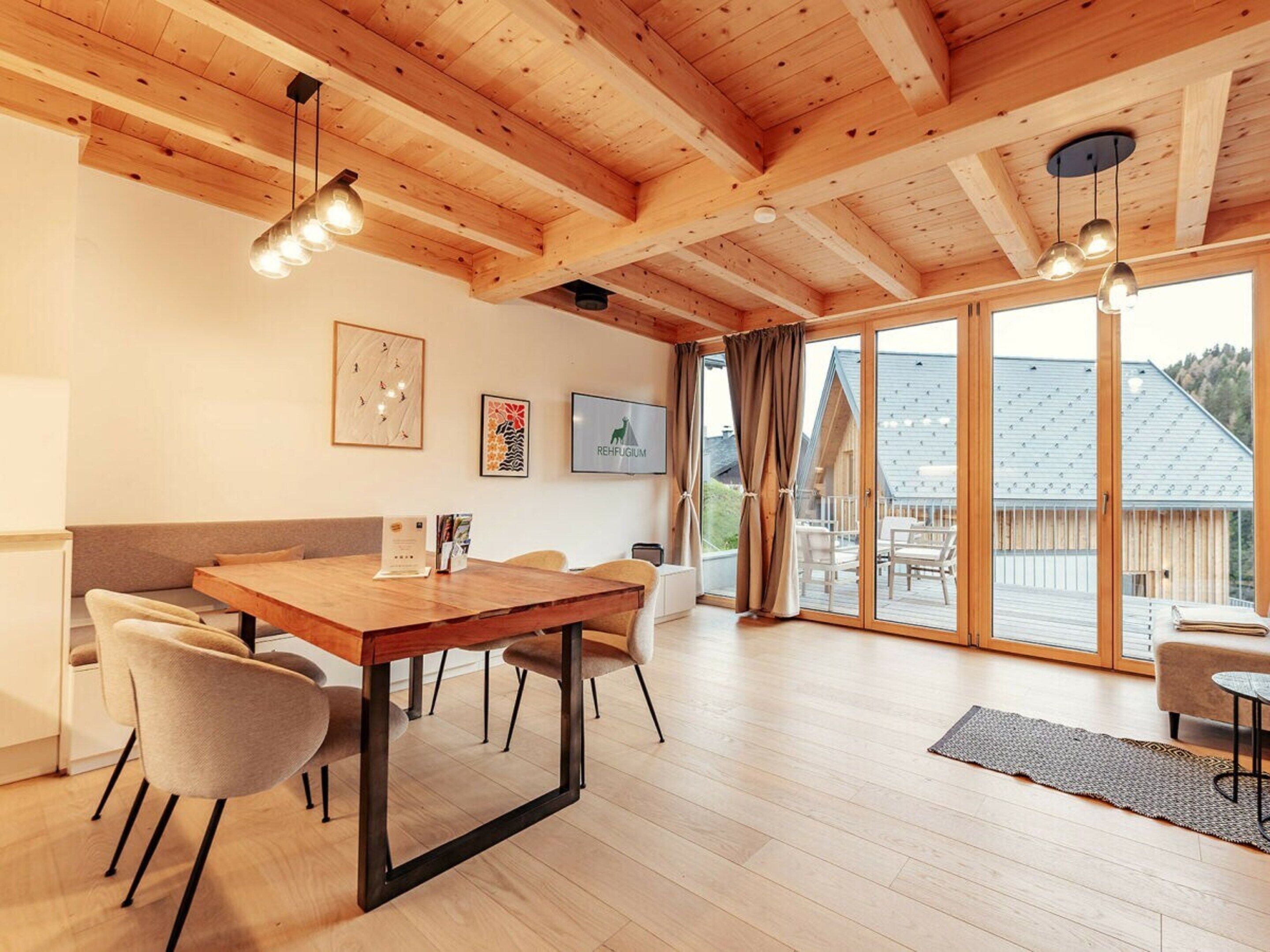 A modern interior with a wooden ceiling, a dining area with a table and chairs, and large sliding glass doors leading to an outdoor deck.