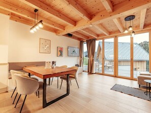 Ein modernes Interieur mit Holzboden, einem Essbereich mit Tisch und Stühlen sowie großen Schiebeglastüren, die auf eine Terrassenfläche führen.