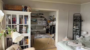 A cozy living room with a sofa, a white cabinet with books, a television, and a bed with a blanket.