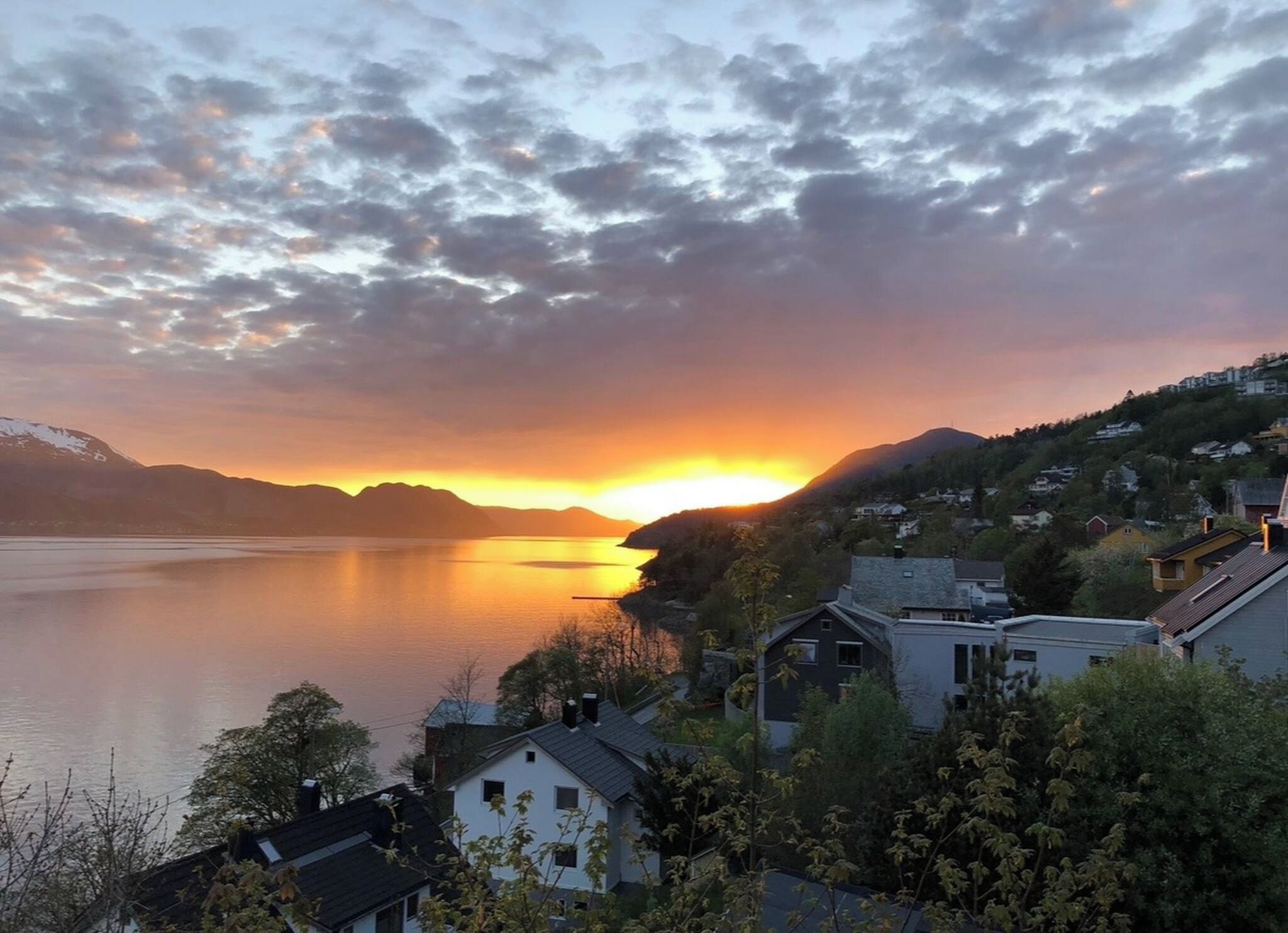 A lakeside view with houses and mountains during sunset.