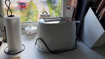 A kitchen counter with a toaster, a cutting board, and a window with a view of houses and a road.