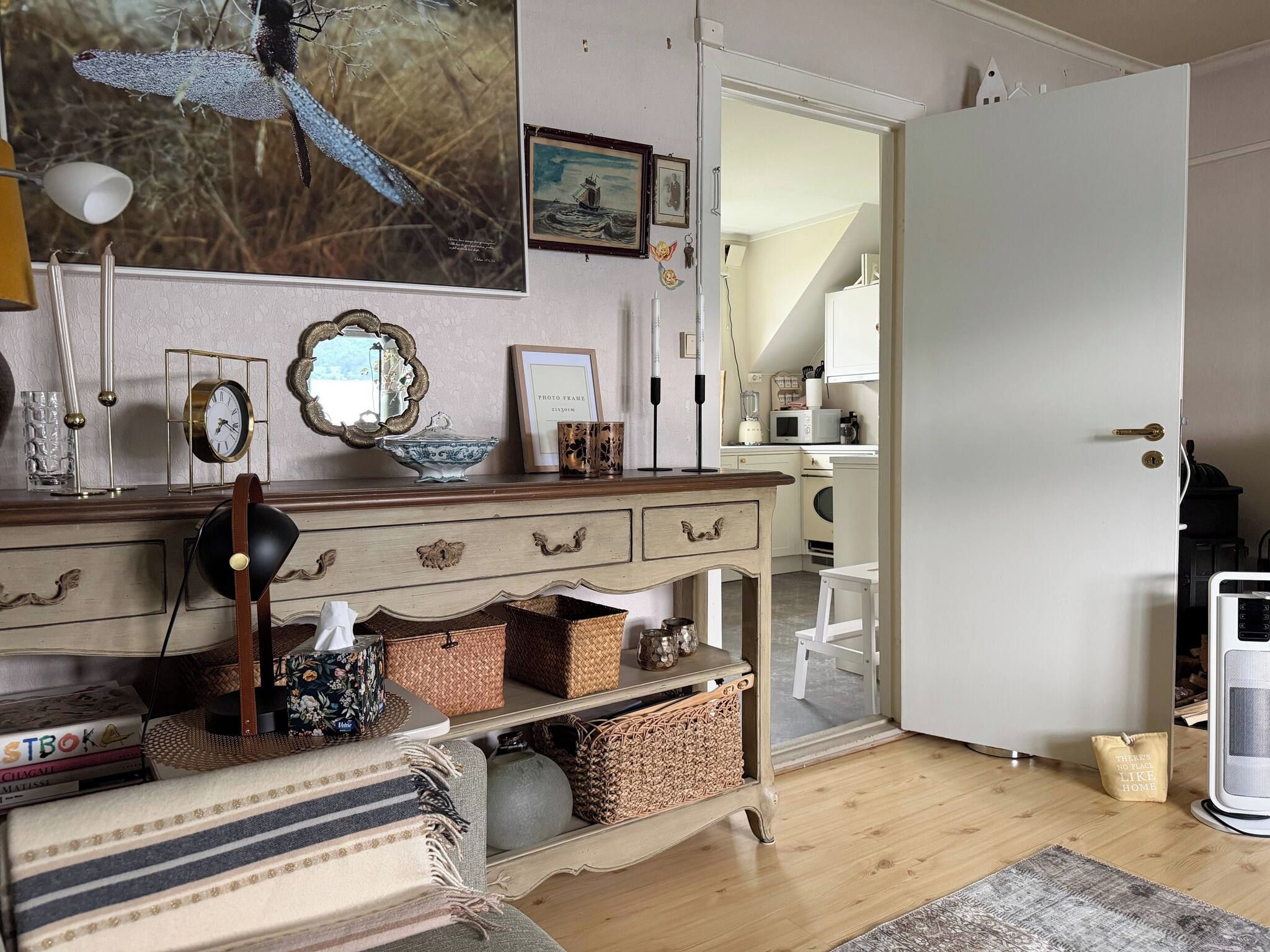 A room with a wooden dresser, a mirror, framed photos, and a white door.
