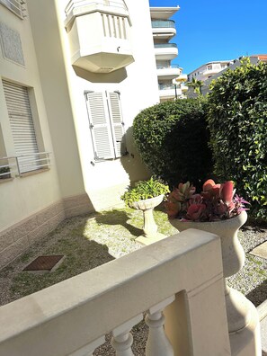 A balcony with a white balustrade, a potted plant, and a small garden area with gravel and grass. - Vrbo Property (Antibes)