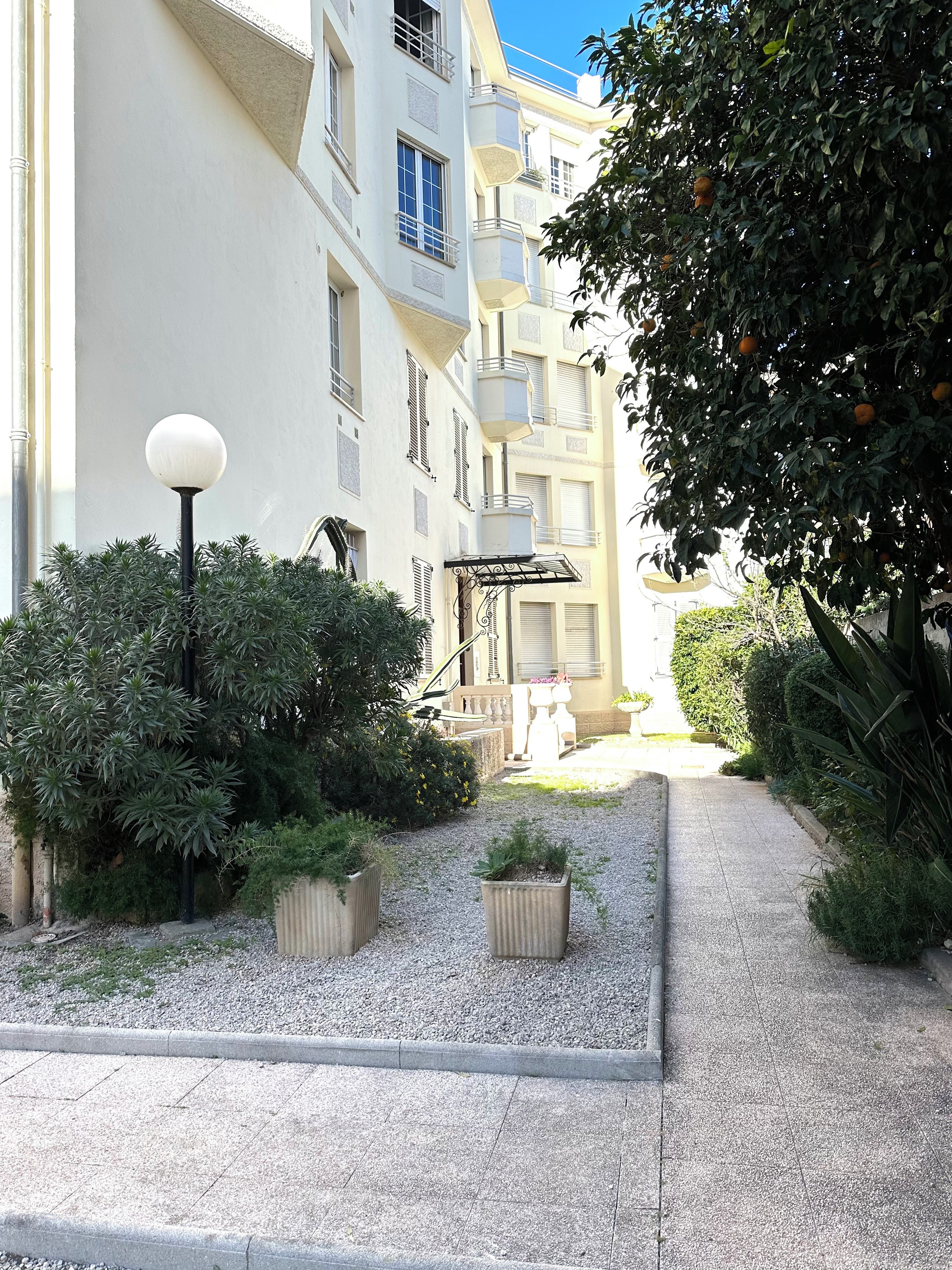A courtyard with a pathway, a street lamp, and a building with balconies.