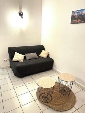 A modern living room with a dark sofa, two round wooden tables, and a wall-mounted light fixture. - Vrbo Property (Antibes)