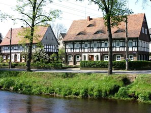 A traditional half-timbered house with a river in the foreground. - Holiday Home With 1 Bedroom (Grossschoenau)