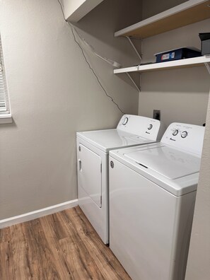 A laundry room with two white washers and dryers, wooden flooring, and a shelf above the dryers. - Awesome 3-bedroom house with AC in vibrant Houston (Houston)