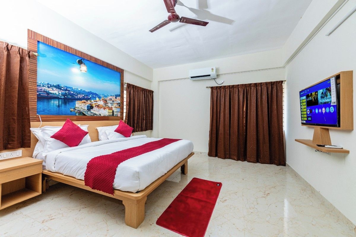 A hotel room with a bed, a television, an air conditioning unit, and a large window with curtains.