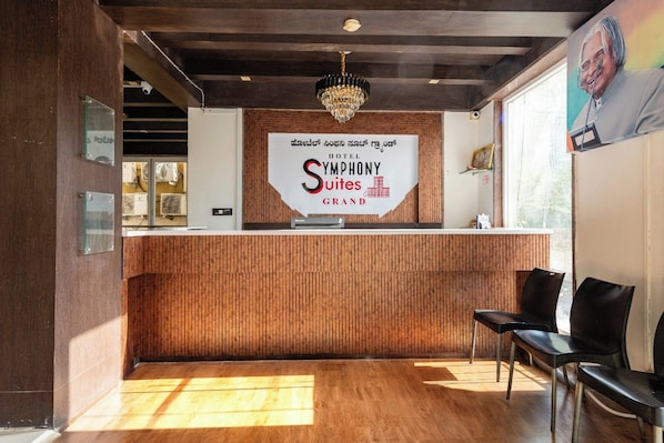 Un mostrador de recepción con un cartel que dice 'Symphony Suites Grand Hotel' y una araña de cristal colgando arriba.