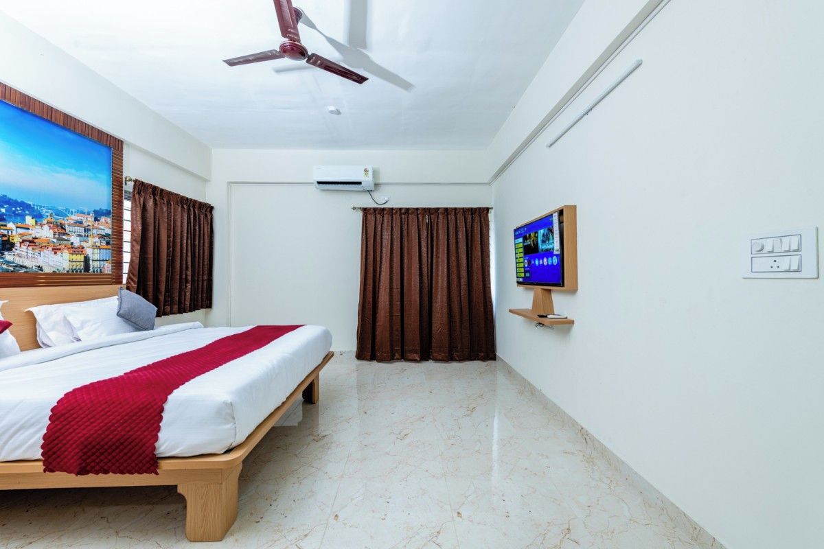 Camera d'albergo con un letto, una ventola a soffitto, un condizionatore d'aria, una televisione su un mobile e vista sulla città attraverso una finestra.