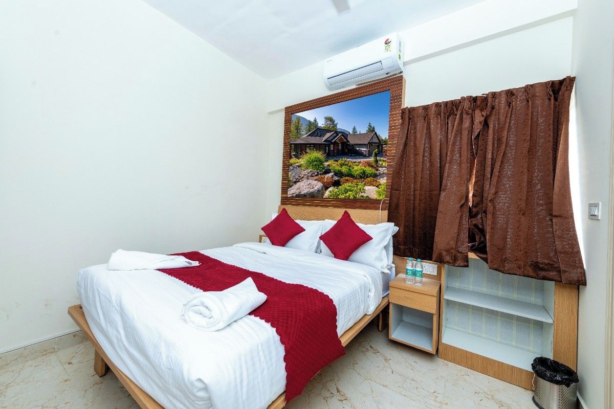 Ein Hotelzimmer mit Bett, Nachttisch, Wand-Klimaanlage und Fenster mit braunen Vorhängen.