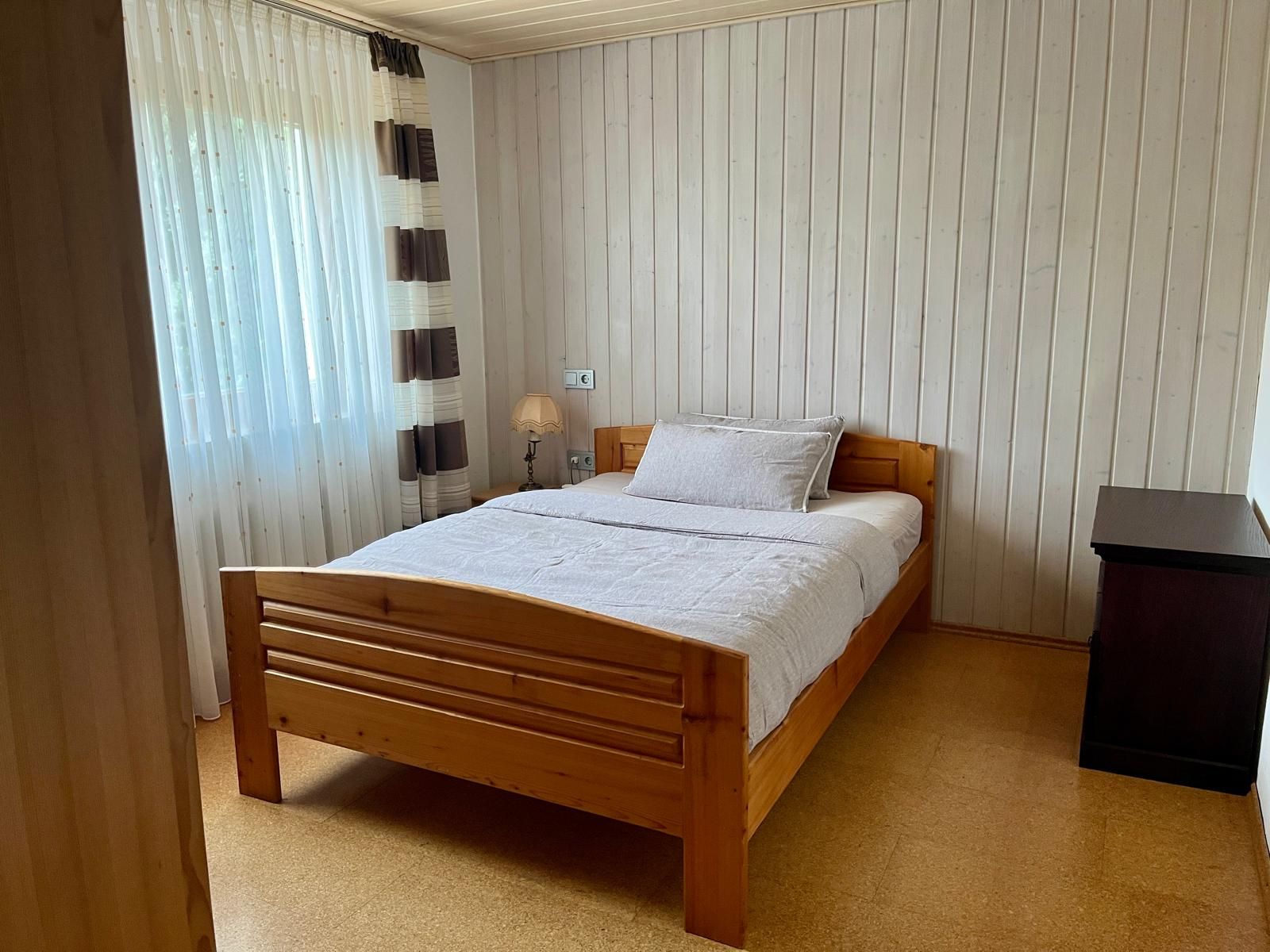 Ein Schlafzimmer mit einem hölzernen Bett, einem Nachttisch, einer Lampe und einer schwarzen Mülltonne.