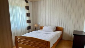 Un dormitorio con una cama de madera, una mesita de noche, una lámpara y un cubo de basura negro.