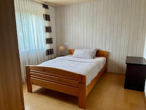 A bedroom with a wooden bed, a nightstand, a lamp, and a black trash bin. - Vrbo Property (Wolfach)