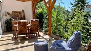 Un patio exterior con muebles de madera, un sillón colgante azul y vistas a un jardín exuberante.