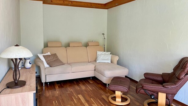 Una sala de estar moderna con un sofá modular, un sillón de cuero marrón, una mesa de centro de madera y una lámpara de pie.
