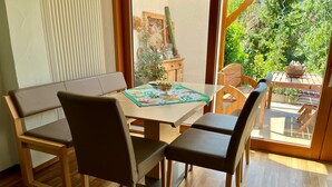 Un comedor con una mesa y sillas de madera, una ventana con vista a follaje y un radiador en la pared.