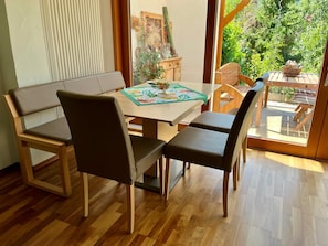 A dining area with a wooden table and chairs, a window with a view of greenery, and a radiator on the wall. - Vrbo Property (Wolfach)