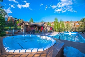 Uma banheira de hidromassagem e uma piscina em um ambiente de resort, com deck de madeira e espreguiçadeiras.