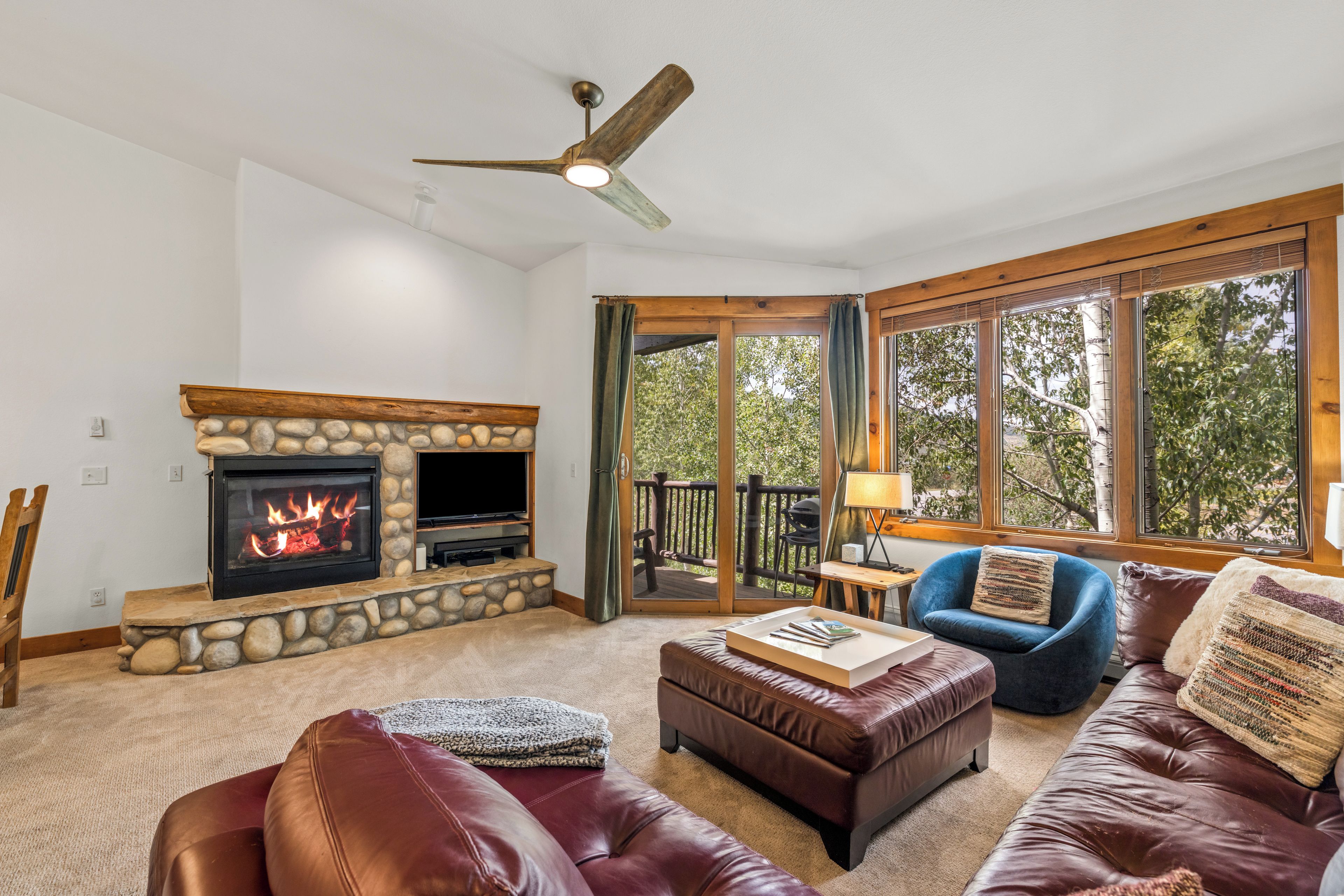 A living room with a stone fireplace, leather furniture, and large windows.