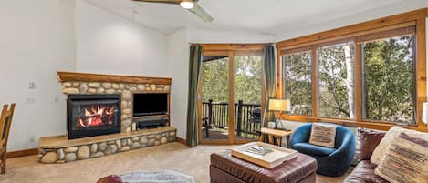 A living room with a stone fireplace, leather furniture, and large windows.